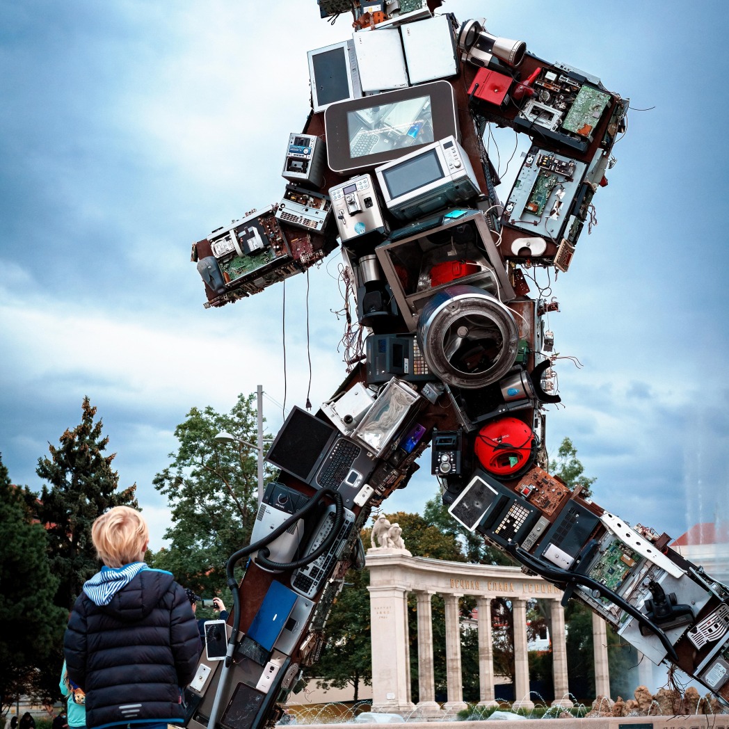 Vaikas stebintis iš elektroninių įrenginių sukonstruotą didelį robotą žingsniuojantį miesto gatve